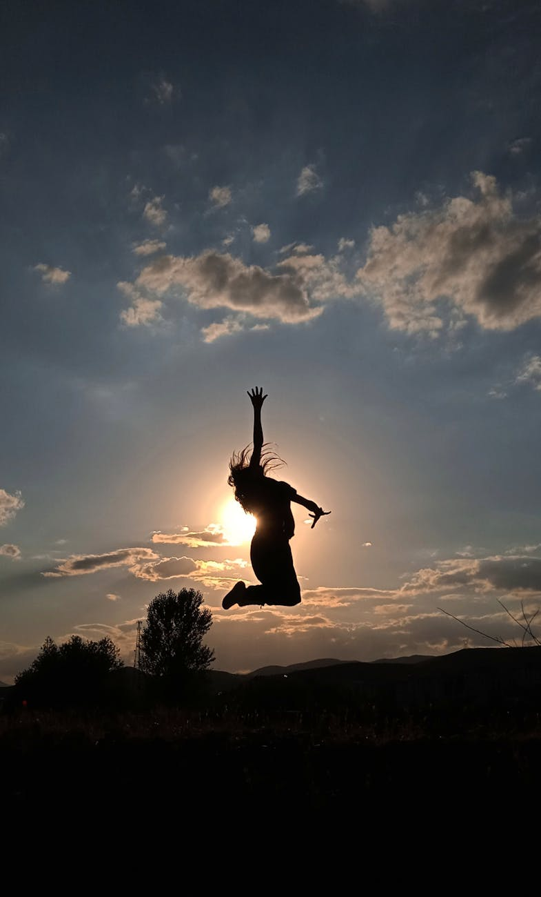 silhouette of woman jumping under cloudy sky